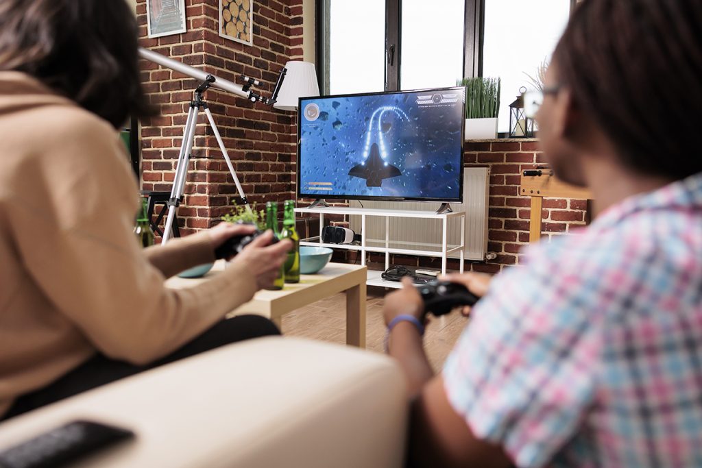 diverse close friends in living room sitting on sofa while playing space sim videogame on gaming device.